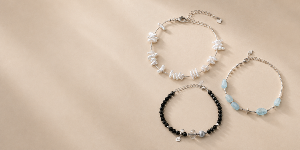 Black onyx, aquamarine and baroque pearl bracelets arranged on a warm neutral background to compare bracelet materials and fit.