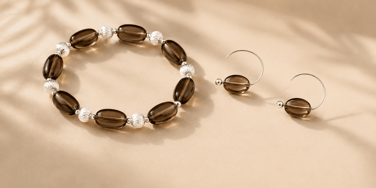 Smoky quartz bracelet and matching hoop earrings arranged on a warm beige surface for LUNARAE's smoky quartz jewelry meaning guide.