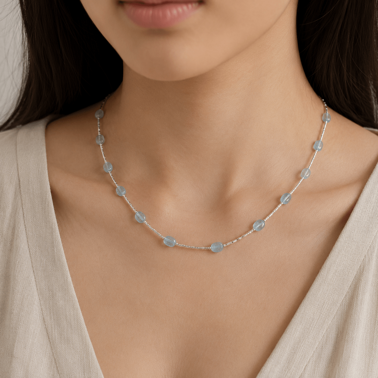 Aquamarine Tube Necklace worn at the collarbone with pale blue aquamarine stones and a soft ivory V-neck top