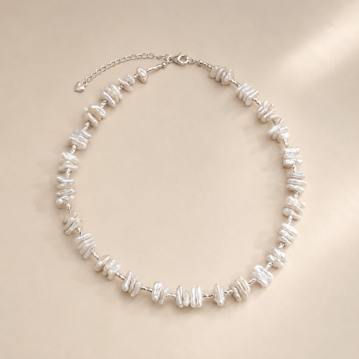 Baroque Pearl Necklace displayed flat on a warm ivory background with irregular white pearls, a twisted silver-toned chain, a spring-ring clasp, and an extender chain
