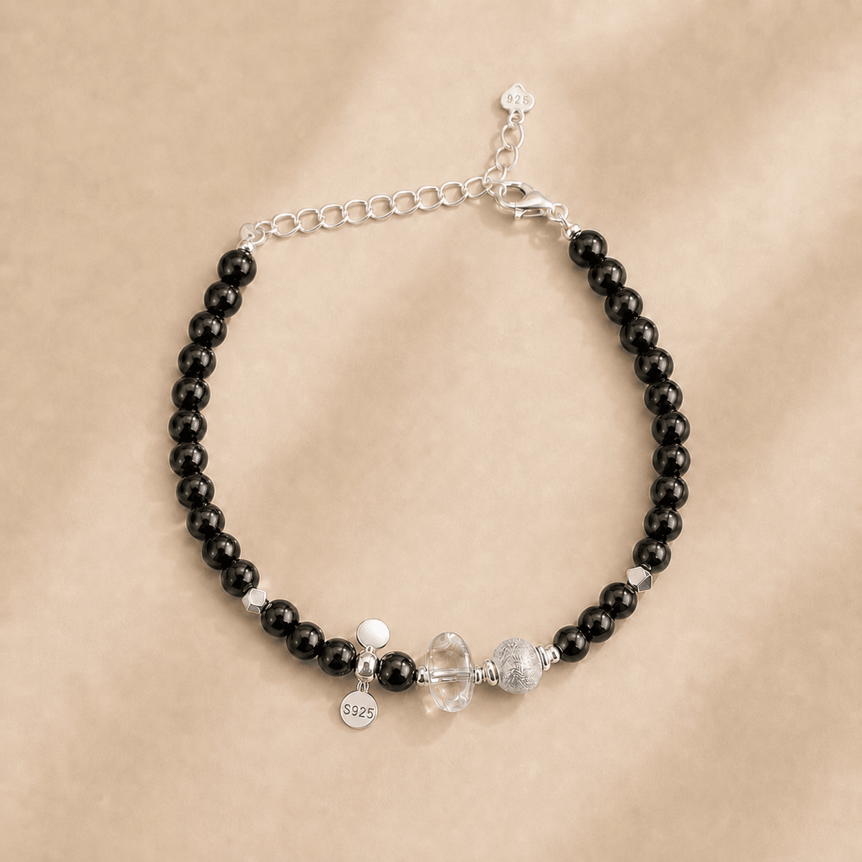 Black Onyx and Clear Quartz Bracelet displayed flat on a warm ivory background with polished black onyx beads, a clear quartz centerpiece, sterling silver details, a lobster clasp, and an extender chain