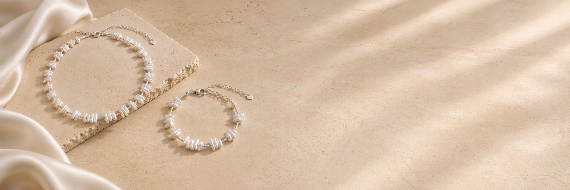 Baroque pearl necklace and matching bracelet styled on warm travertine with soft ivory satin and natural light.