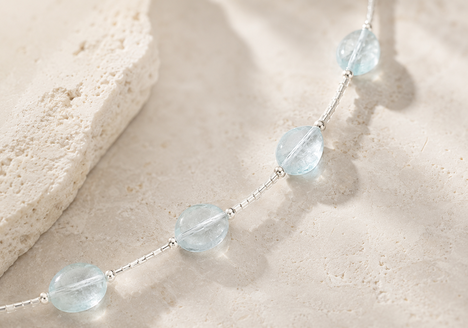 Close-up of natural aquamarine stones and 925 sterling silver details on a warm textured surface, showing subtle variations in color and clarity.