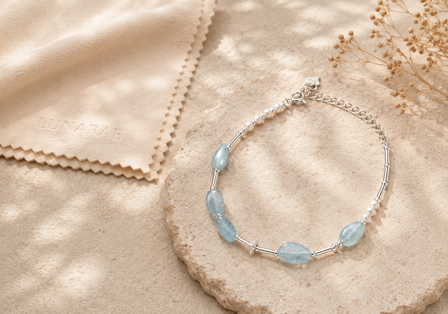 Aquamarine and pearl necklace arranged on warm textured stone beside an embossed LUNARAE jewelry care cloth