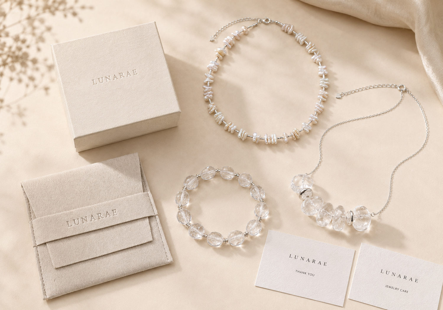 LUNARAE clear quartz necklace, clear quartz bracelet, baroque pearl necklace, jewelry box, pouch, and care cards arranged on a warm beige background.