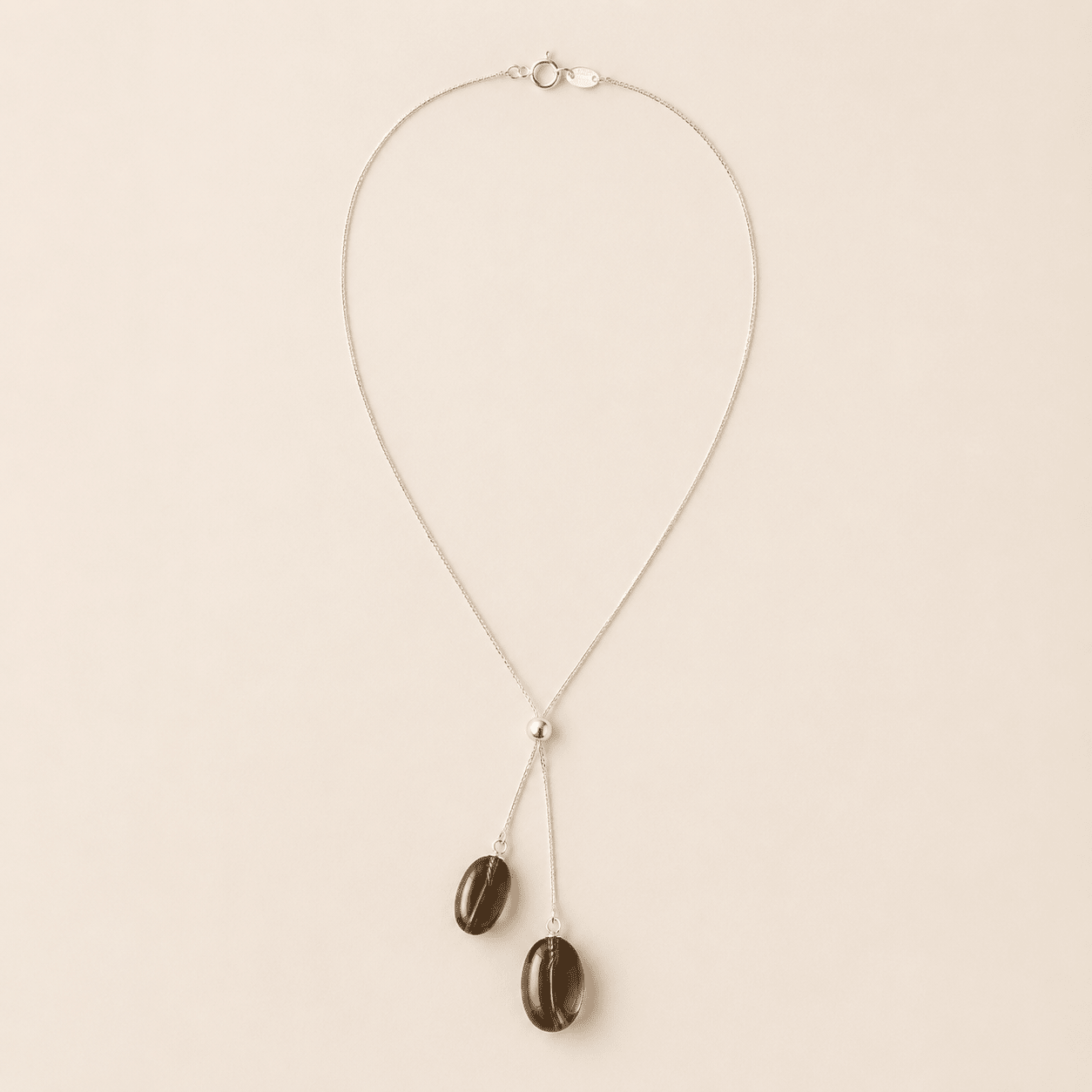 Smoky Quartz Y Necklace displayed flat on a warm ivory background with two oval smoky quartz drops, a polished silver slider bead, and a fine silver chain