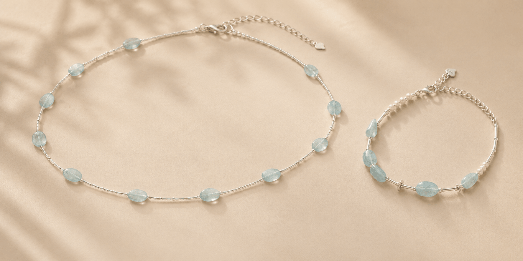 Aquamarine silver necklace and matching aquamarine pearl bracelet arranged on a warm beige surface for LUNARAE's aquamarine jewelry meaning guide.