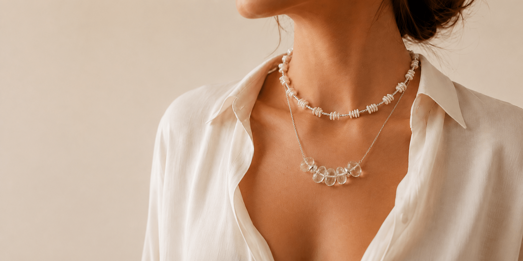 Woman wearing layered baroque pearl and clear quartz necklaces with an ivory blouse