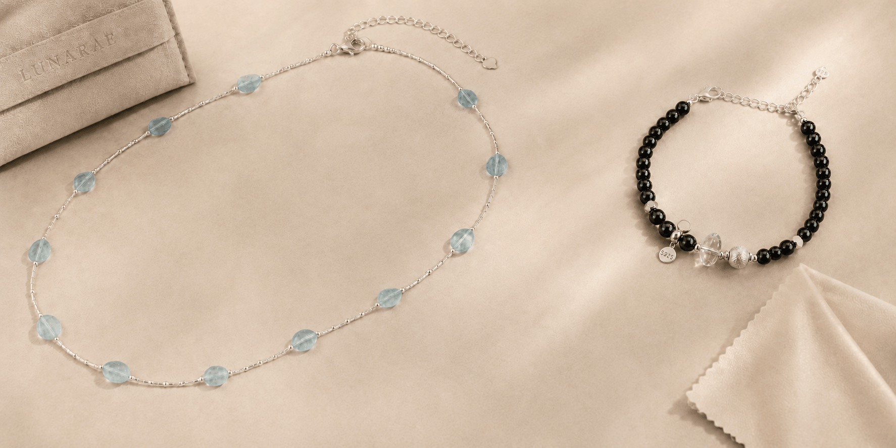 Aquamarine necklace and black onyx bracelet arranged with a LUNARAE jewelry pouch and polishing cloth on a warm beige background.