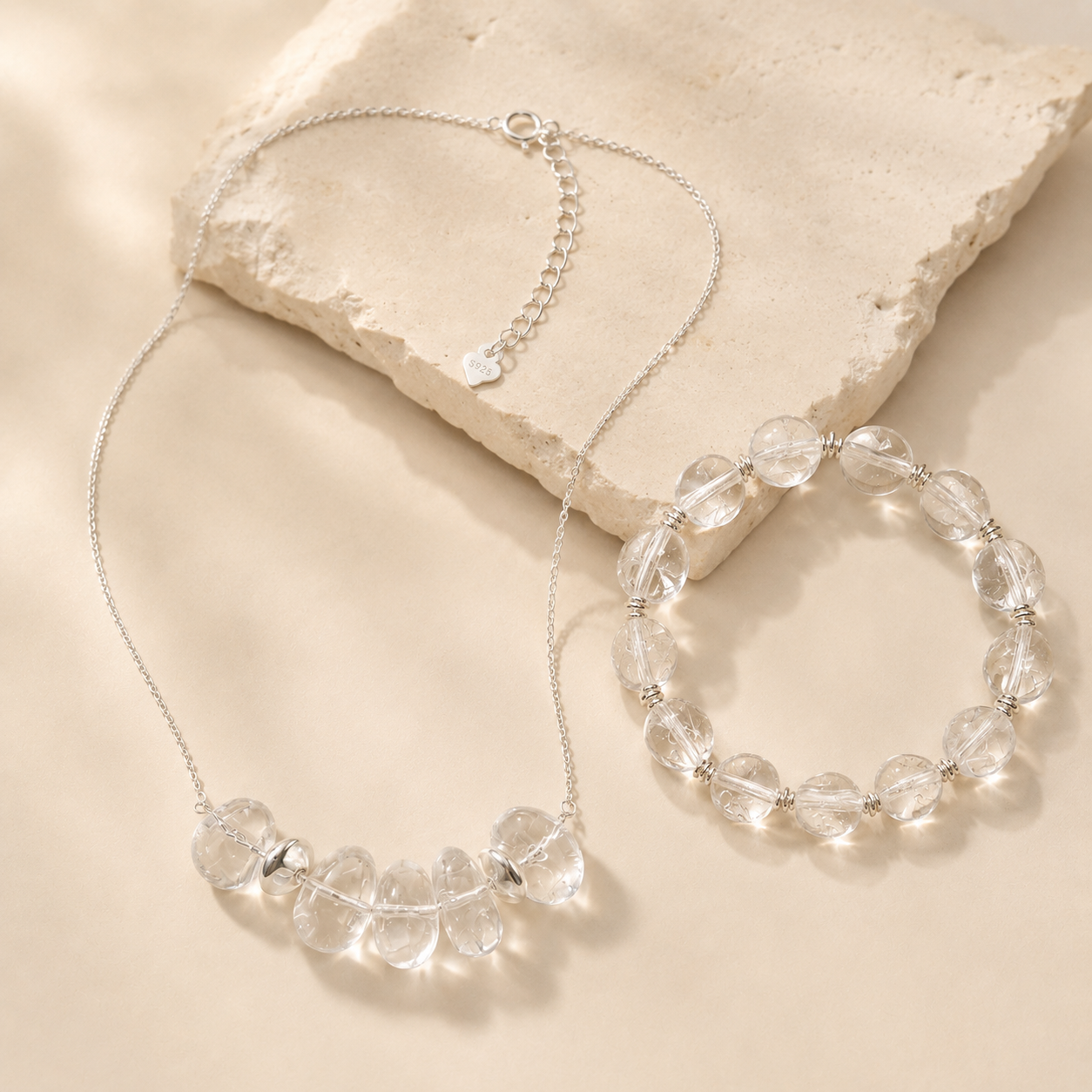 Clear quartz necklace and bracelet arranged on warm ivory stone for the LUNARAE Clarity collection.