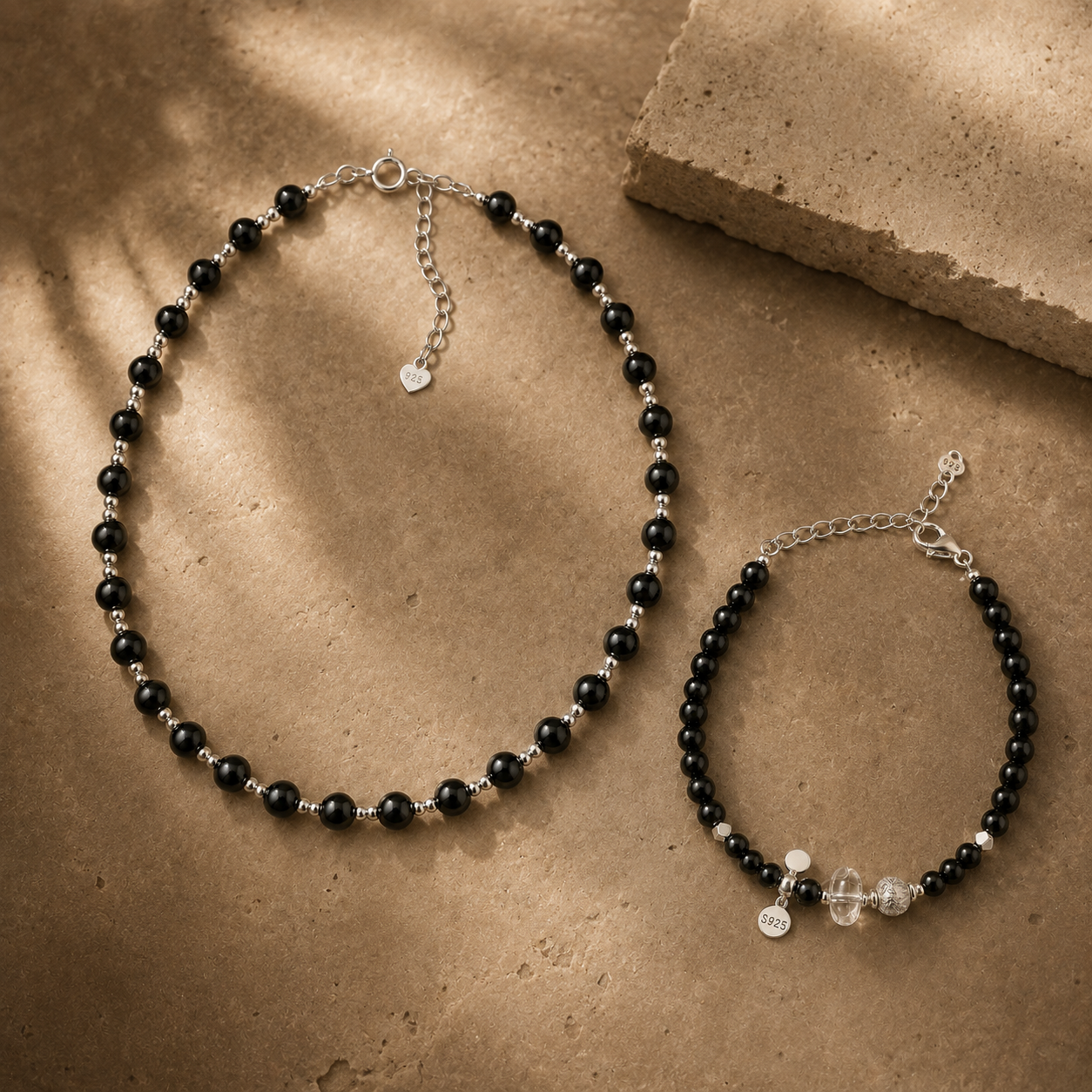 Black onyx necklace and bracelet styled on a warm textured surface for the LUNARAE Protection collection.