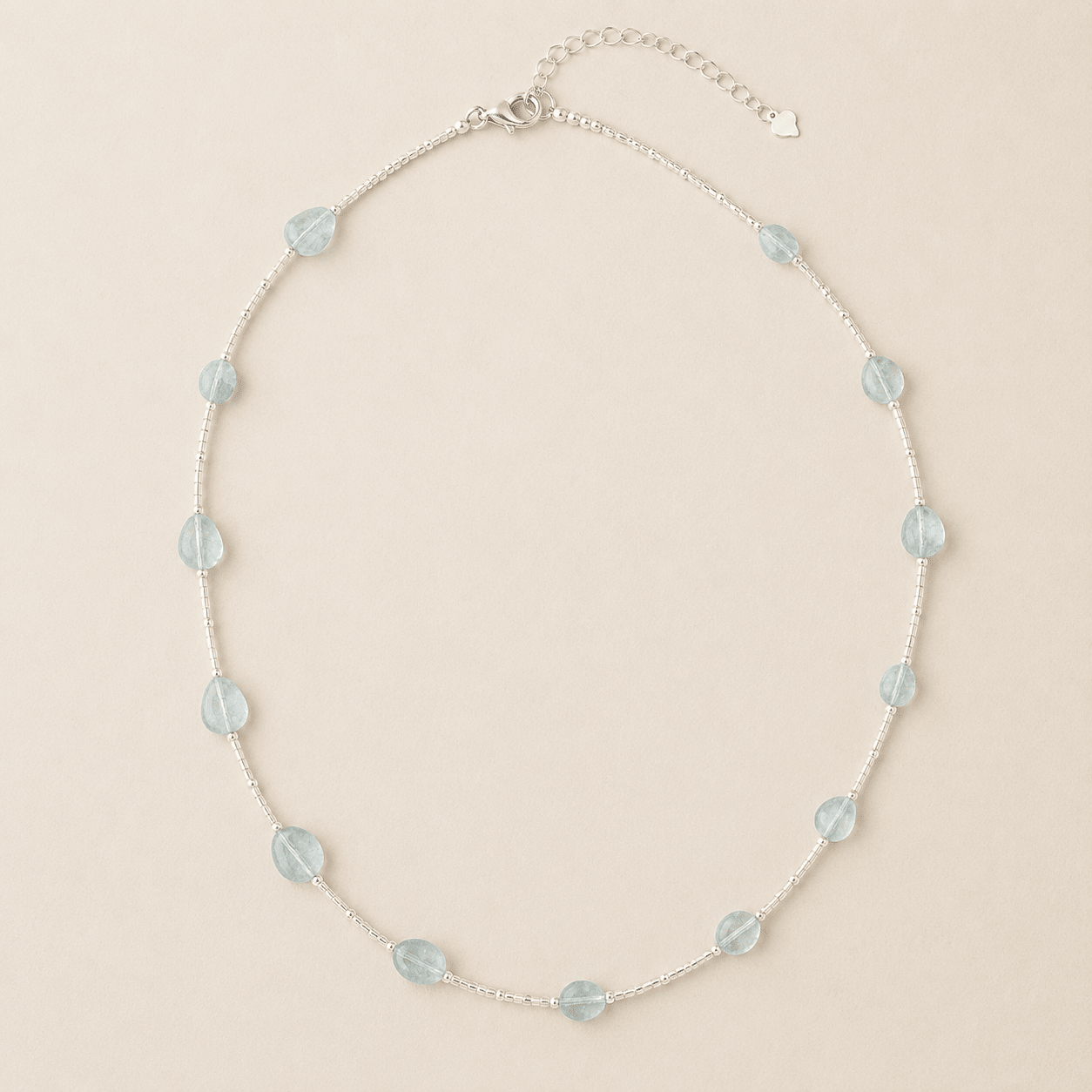 Aquamarine Tube Necklace displayed flat on a warm ivory background with pale blue aquamarine stones, silver tube beads, a lobster clasp, and an extender chain