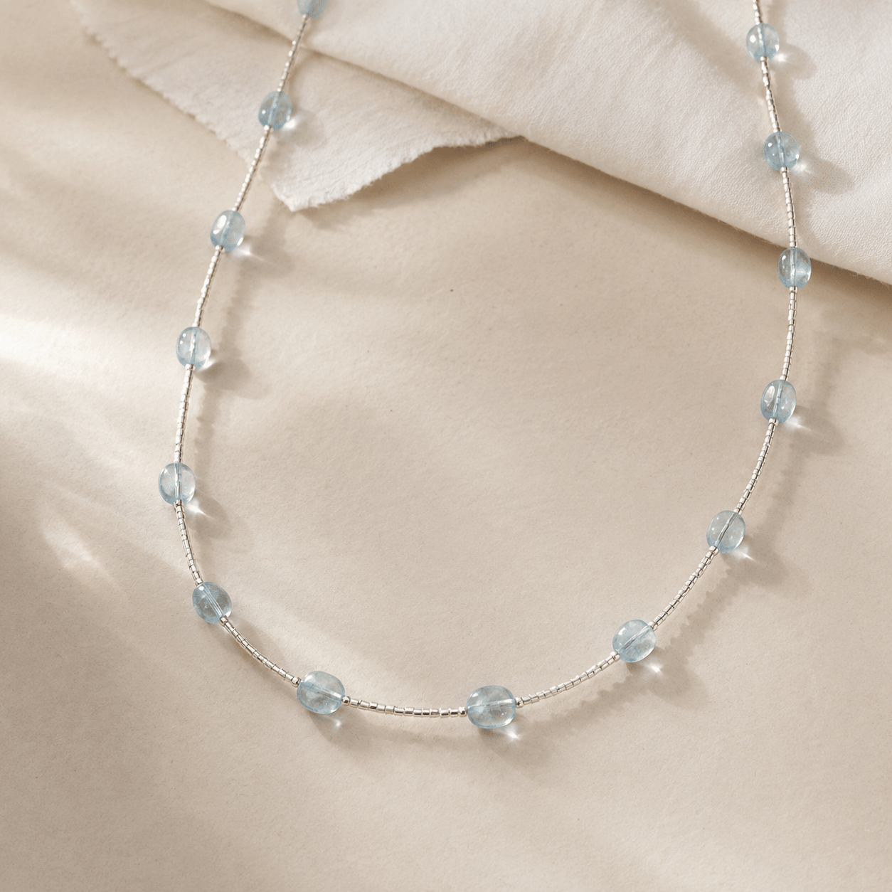 Aquamarine Tube Necklace arranged on layered ivory fabric, showing the evenly spaced aquamarine stones and silver tube beadwork