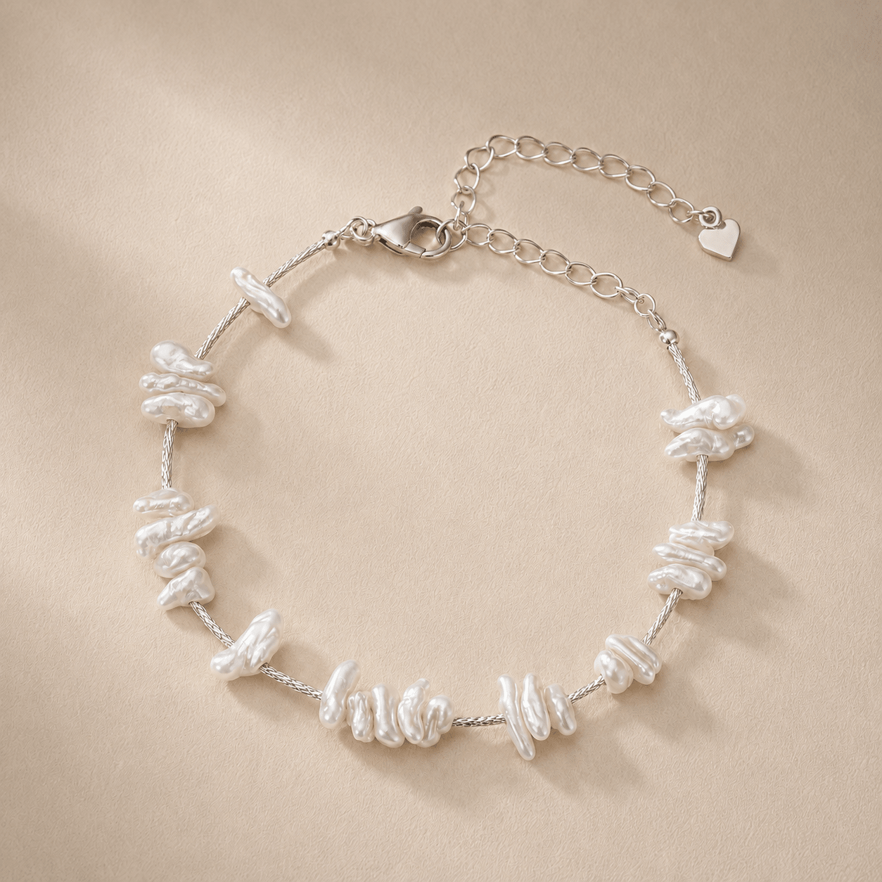 Baroque Pearl Bracelet displayed flat on a warm ivory background with irregular natural baroque pearls, a sterling silver braided chain, a lobster clasp, and an extender chain with a heart charm
