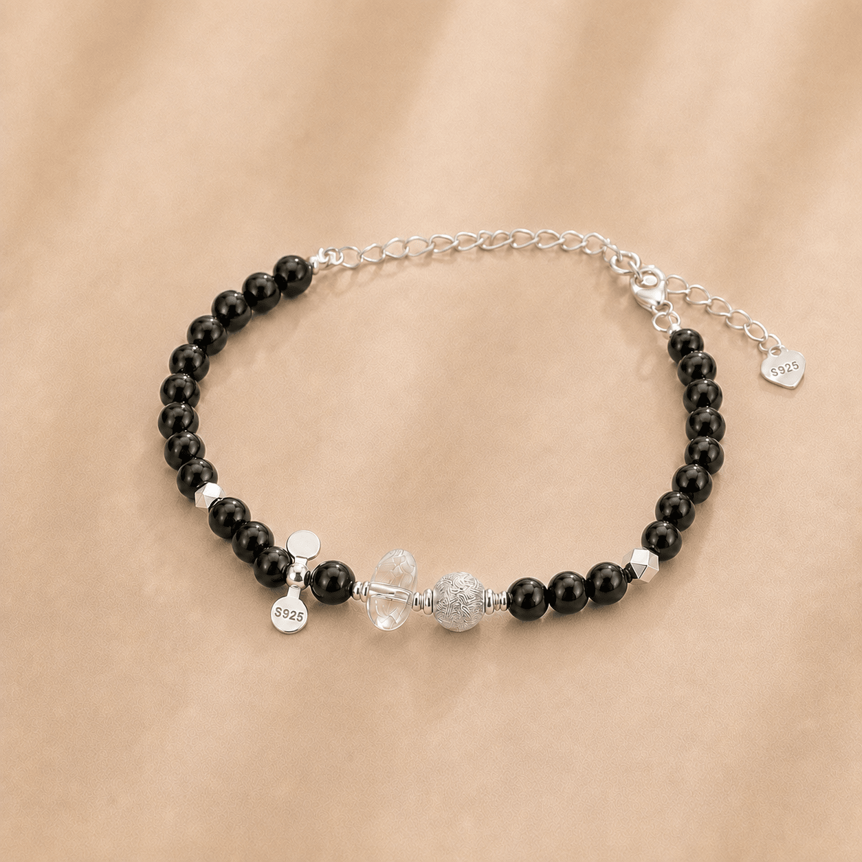Black Onyx and Clear Quartz Bracelet shown from an alternate flat-lay angle with the extender chain, S925 heart tag, clear quartz centerpiece, and decorative silver beads visible
