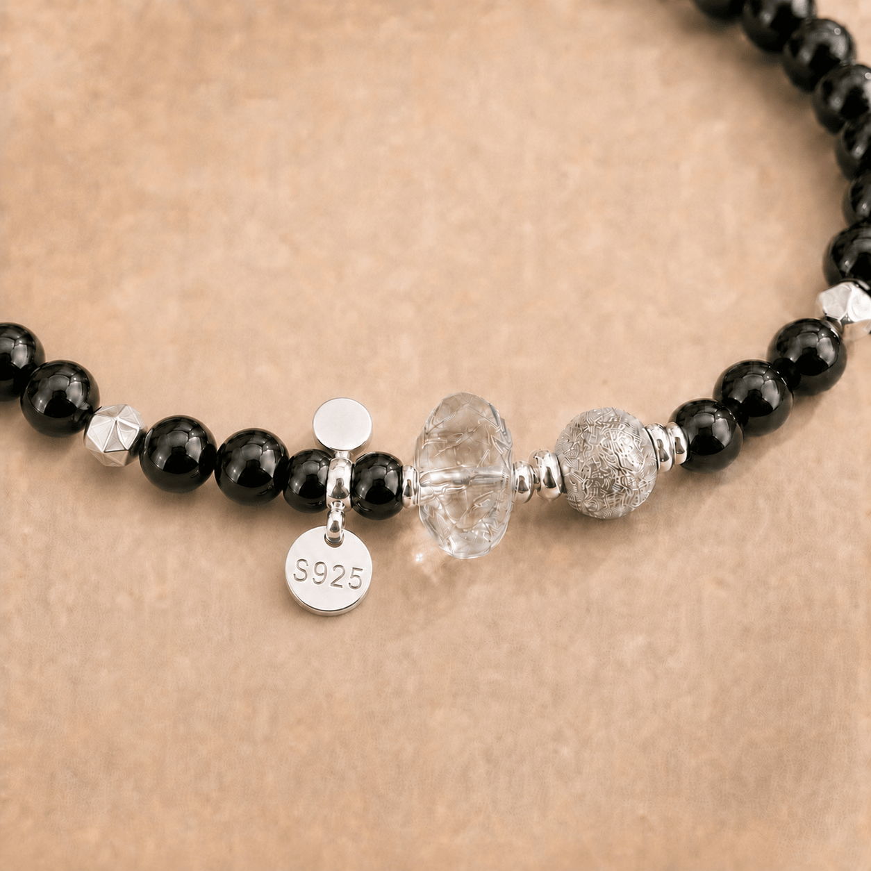 Close-up of the Black Onyx and Clear Quartz Bracelet showing polished black onyx beads, a carved clear quartz centerpiece, textured sterling silver bead, and S925 charm