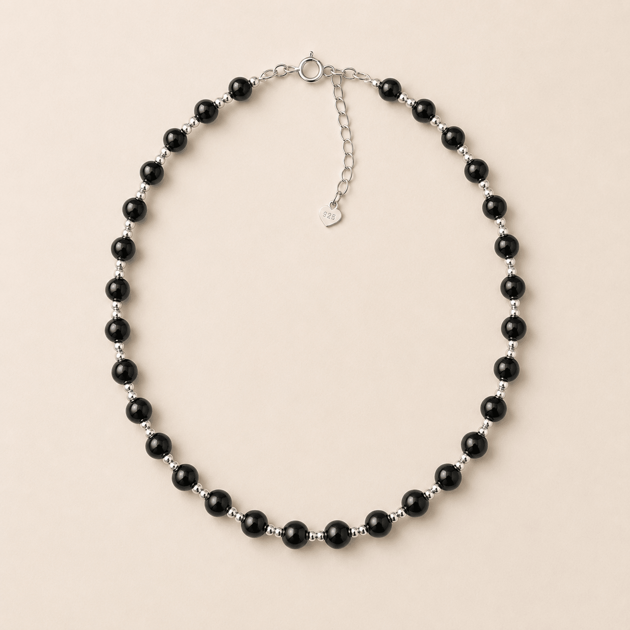 Black Onyx Bead Necklace displayed flat on a warm ivory background with polished black onyx beads, sterling silver spacer beads, a spring-ring clasp, and an extender chain
