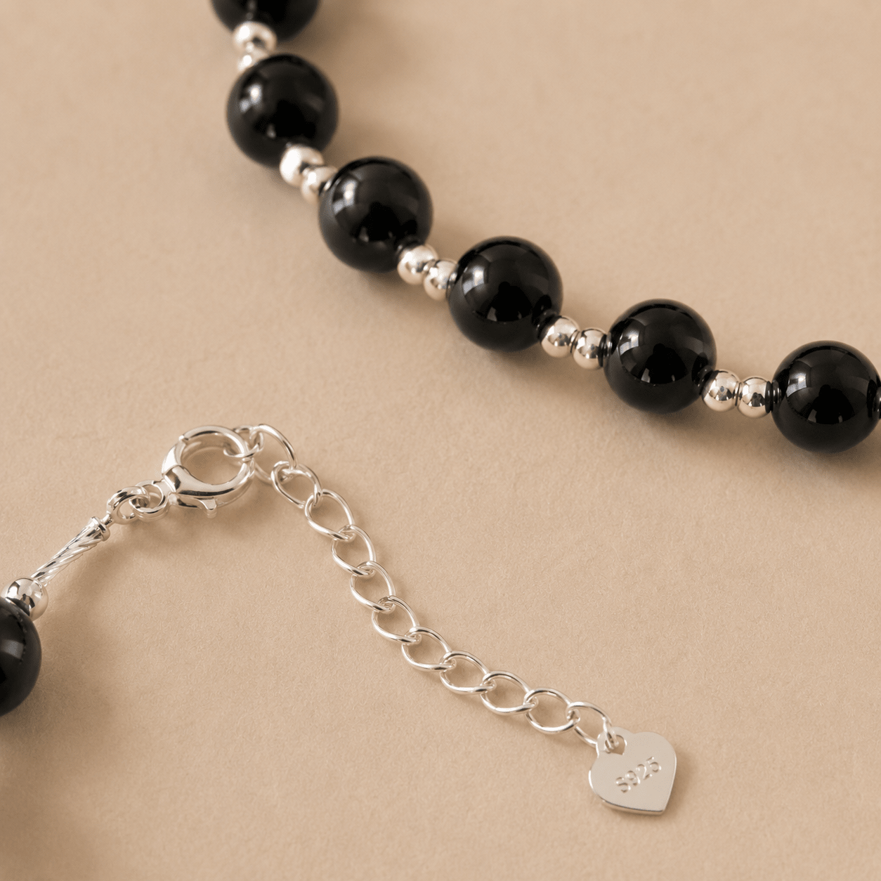 Close-up of the Black Onyx Bead Necklace showing polished black onyx beads, sterling silver spacer beads, the clasp, and the extender chain with an S925 heart tag