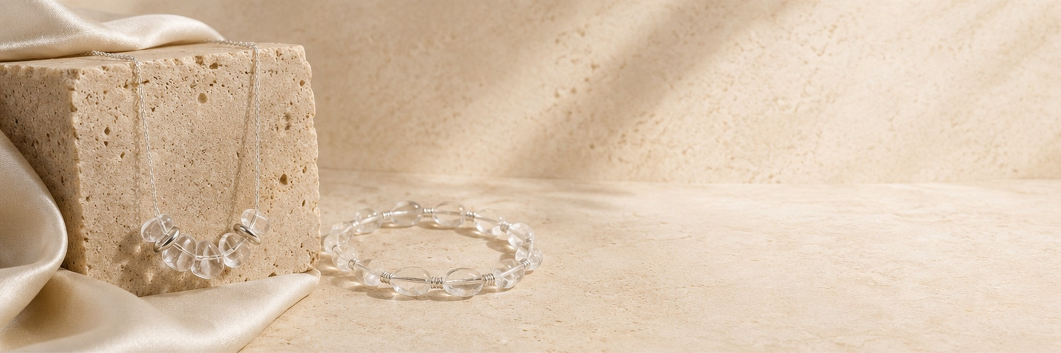 Clear quartz necklace and bracelet displayed on warm travertine stone with soft ivory fabric.