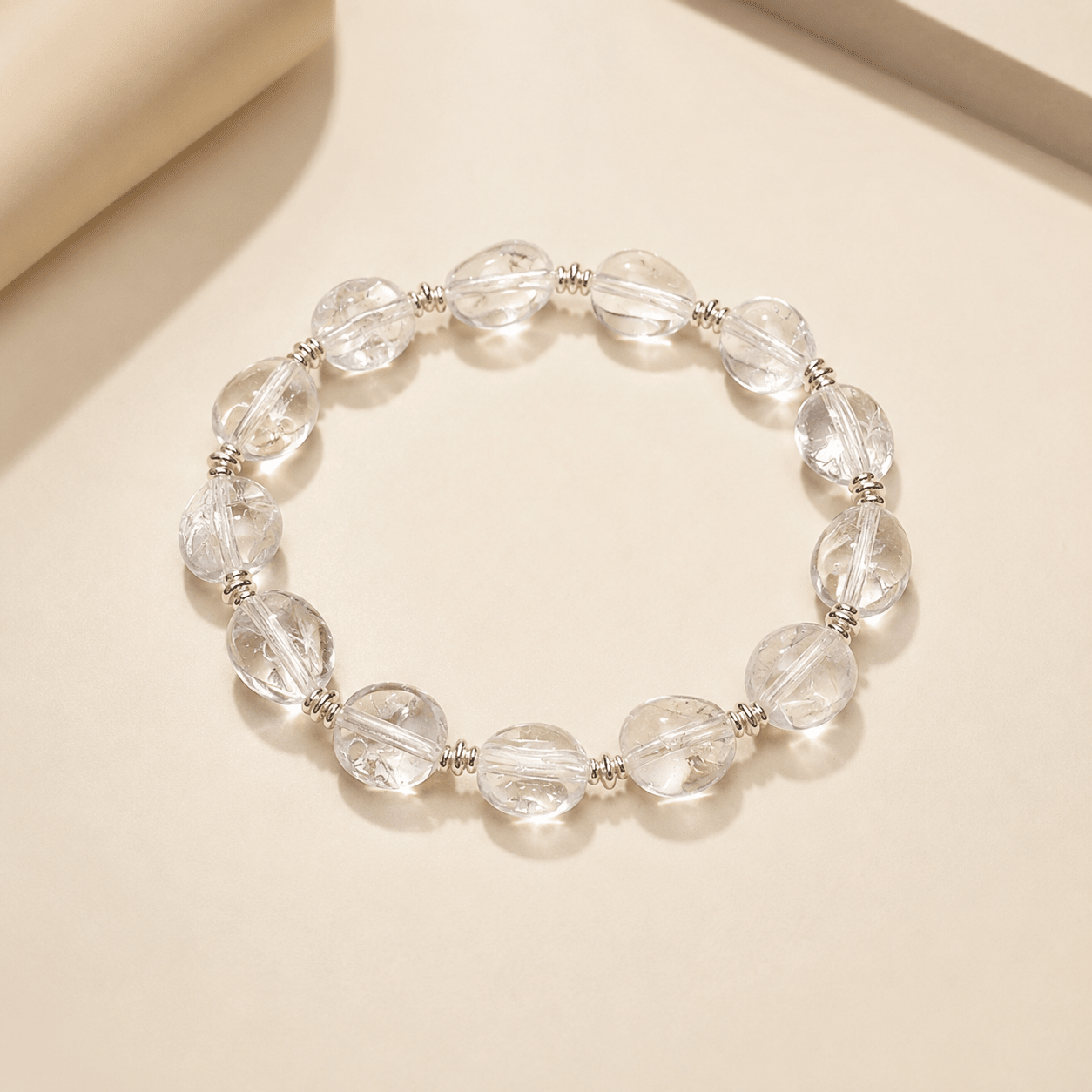Clear Quartz Silver Bead Bracelet displayed flat on a warm ivory background with polished round clear quartz beads and sterling silver spacer details