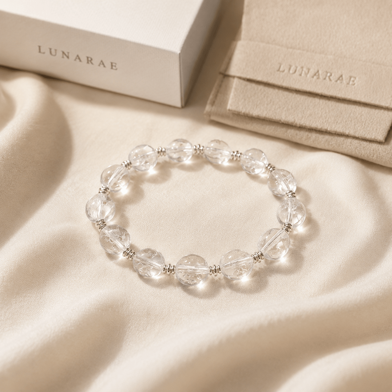 Clear Quartz Silver Bead Bracelet styled on soft ivory fabric with LUNARAE packaging elements in the background