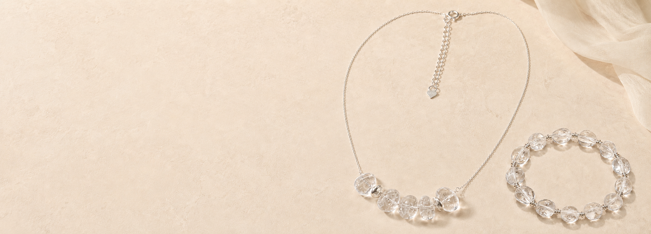 Clear quartz necklace and bracelet styled on a warm beige surface for the LUNARAE homepage hero