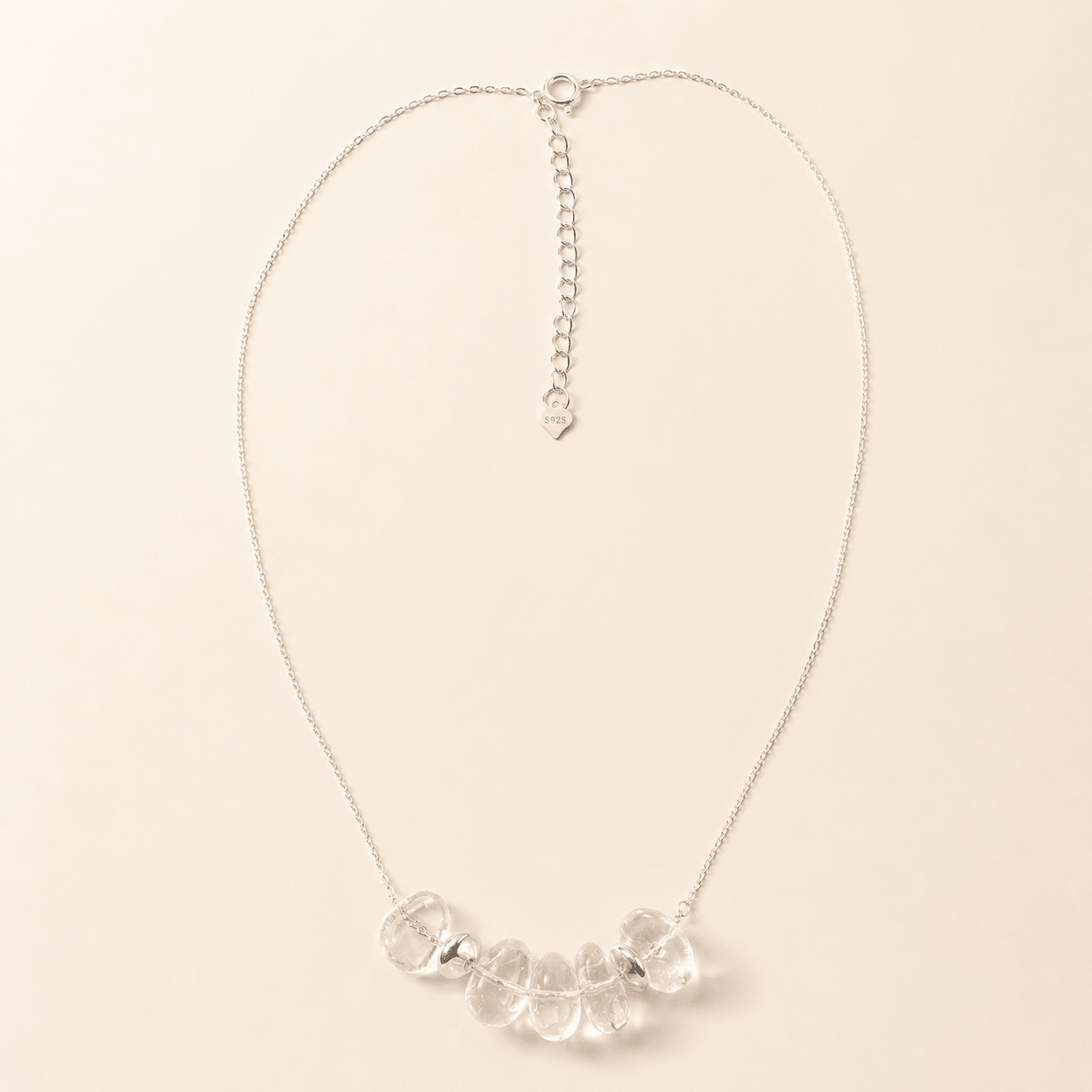 Clear Quartz Pendant Necklace displayed flat on a warm ivory background with five irregular clear quartz stones, sterling silver spacers, and a fine silver chain