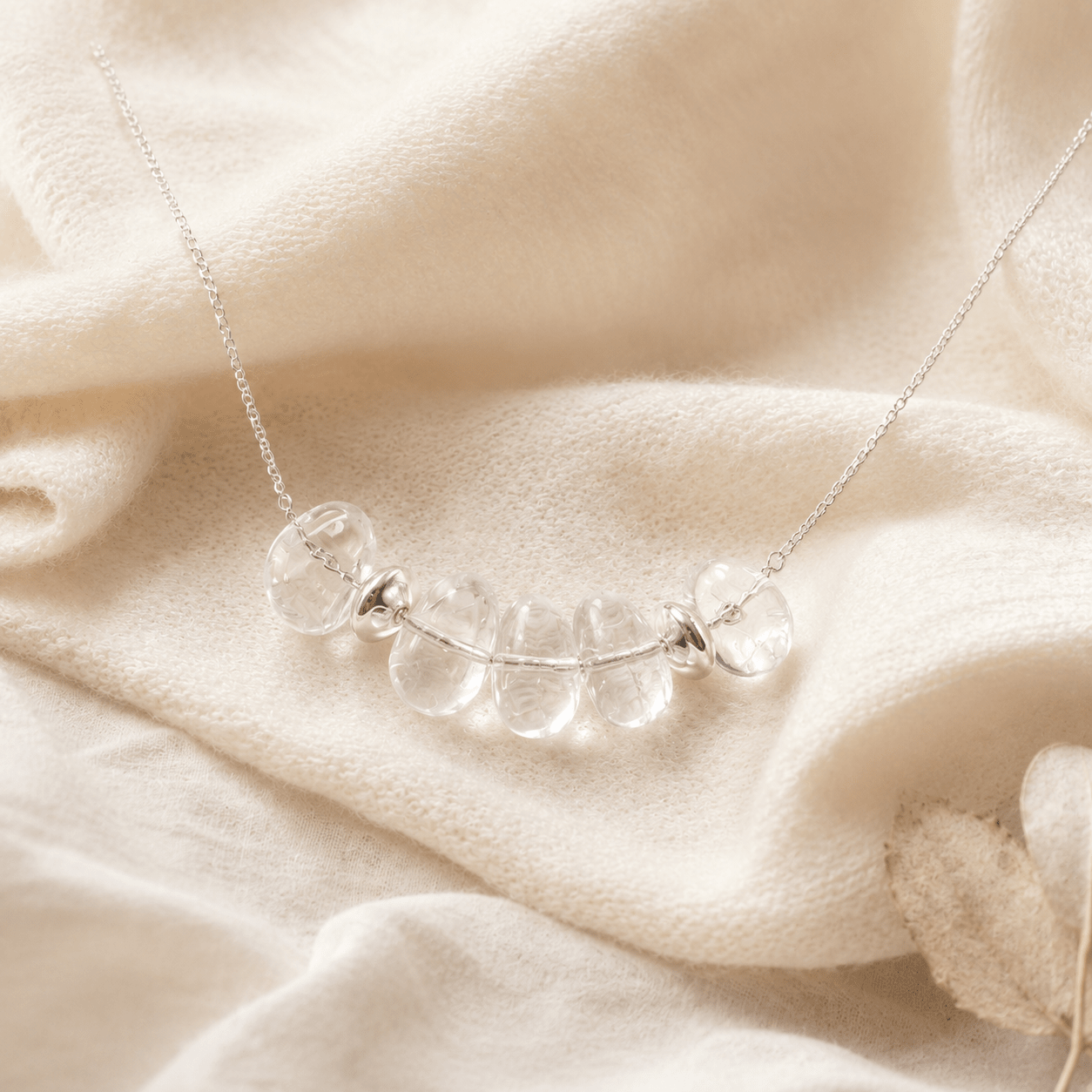 Clear Quartz Pendant Necklace styled on soft cream knit fabric in a warm neutral setting