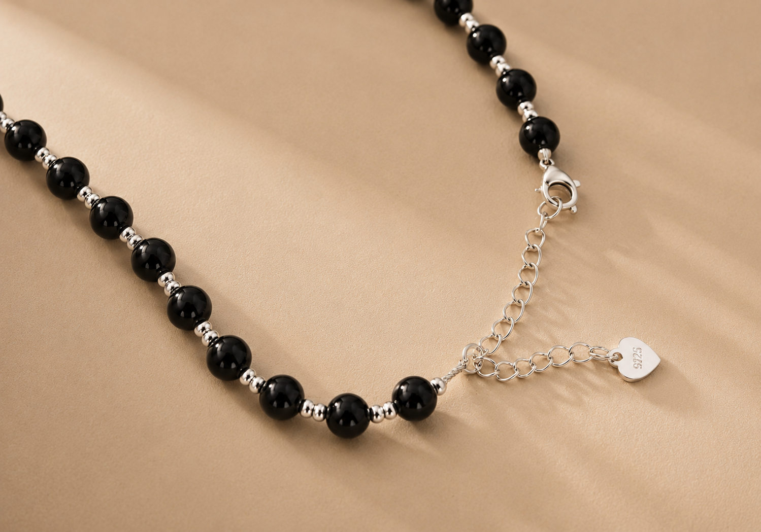 Close-up of a black onyx necklace with paired 925 Sterling Silver spacer beads, clasp, extender chain, and heart-shaped 925 tag.