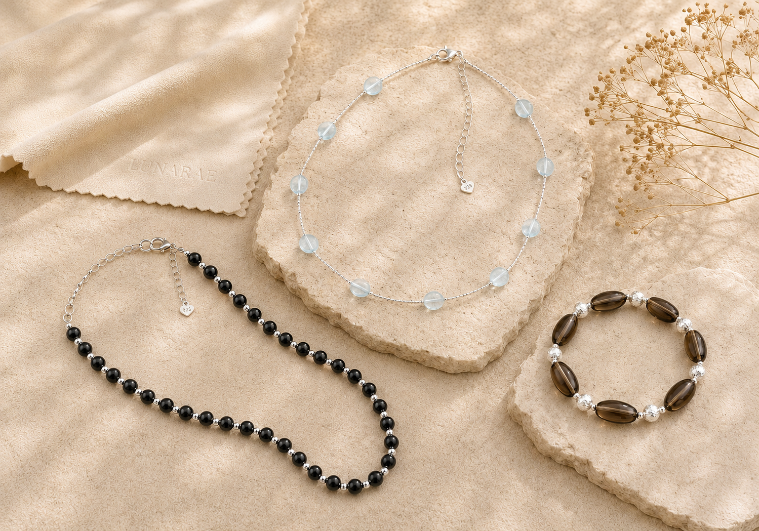 Black onyx necklace, aquamarine necklace, and smoky quartz bracelet arranged on warm natural stone for jewelry care