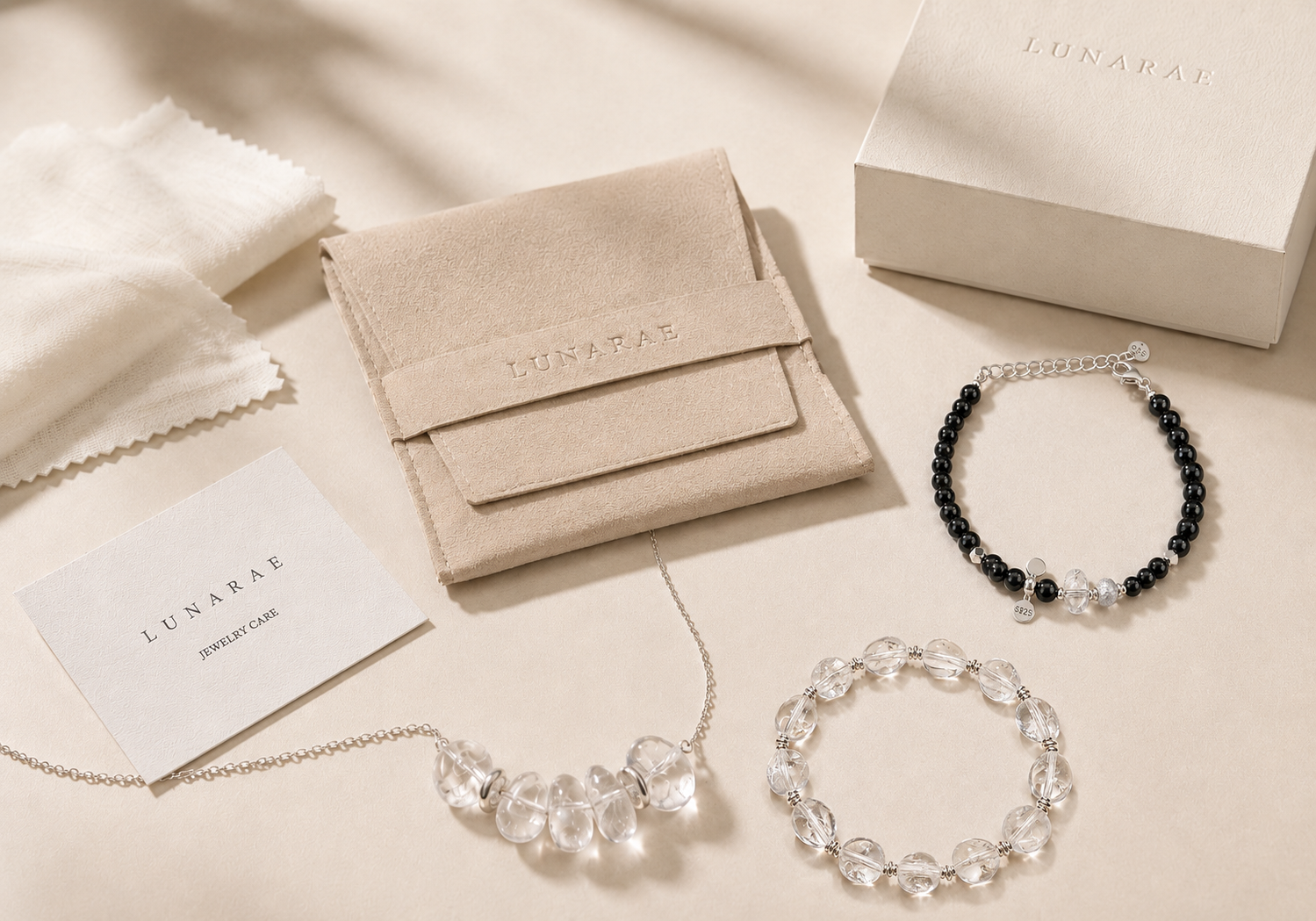 LUNARAE natural stone jewelry care flat lay with clear quartz necklace, clear quartz bracelet, black onyx bracelet, storage pouch, jewelry box, and care card.