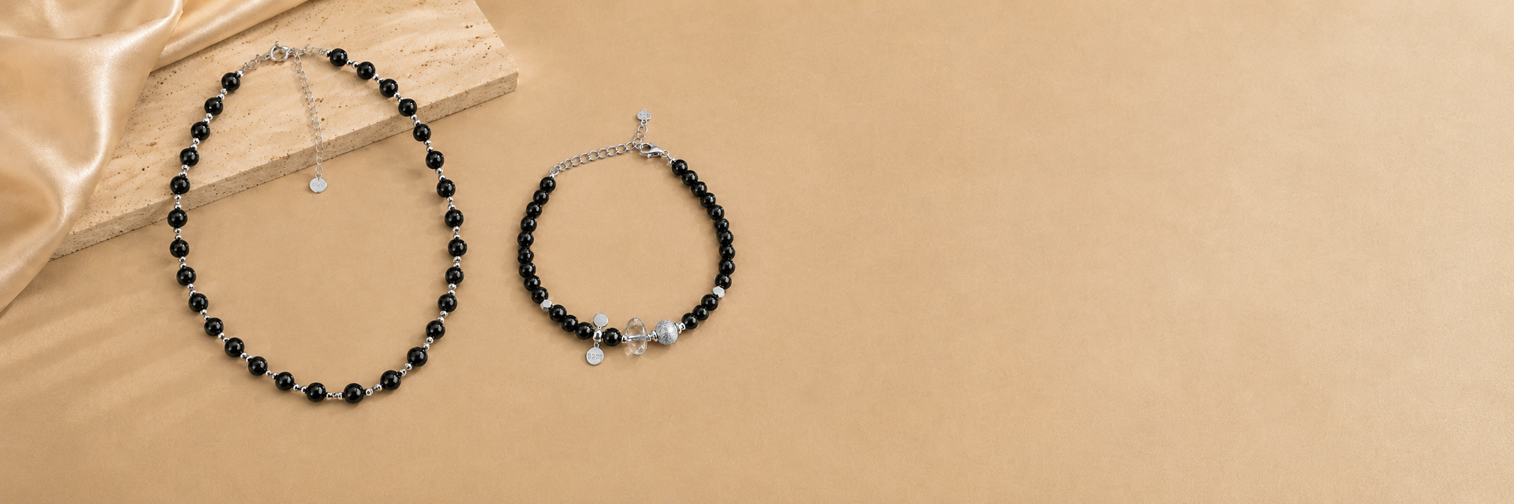 LUNARAE Protection Collection with a black onyx necklace and black onyx clear quartz bracelet on warm beige stone.