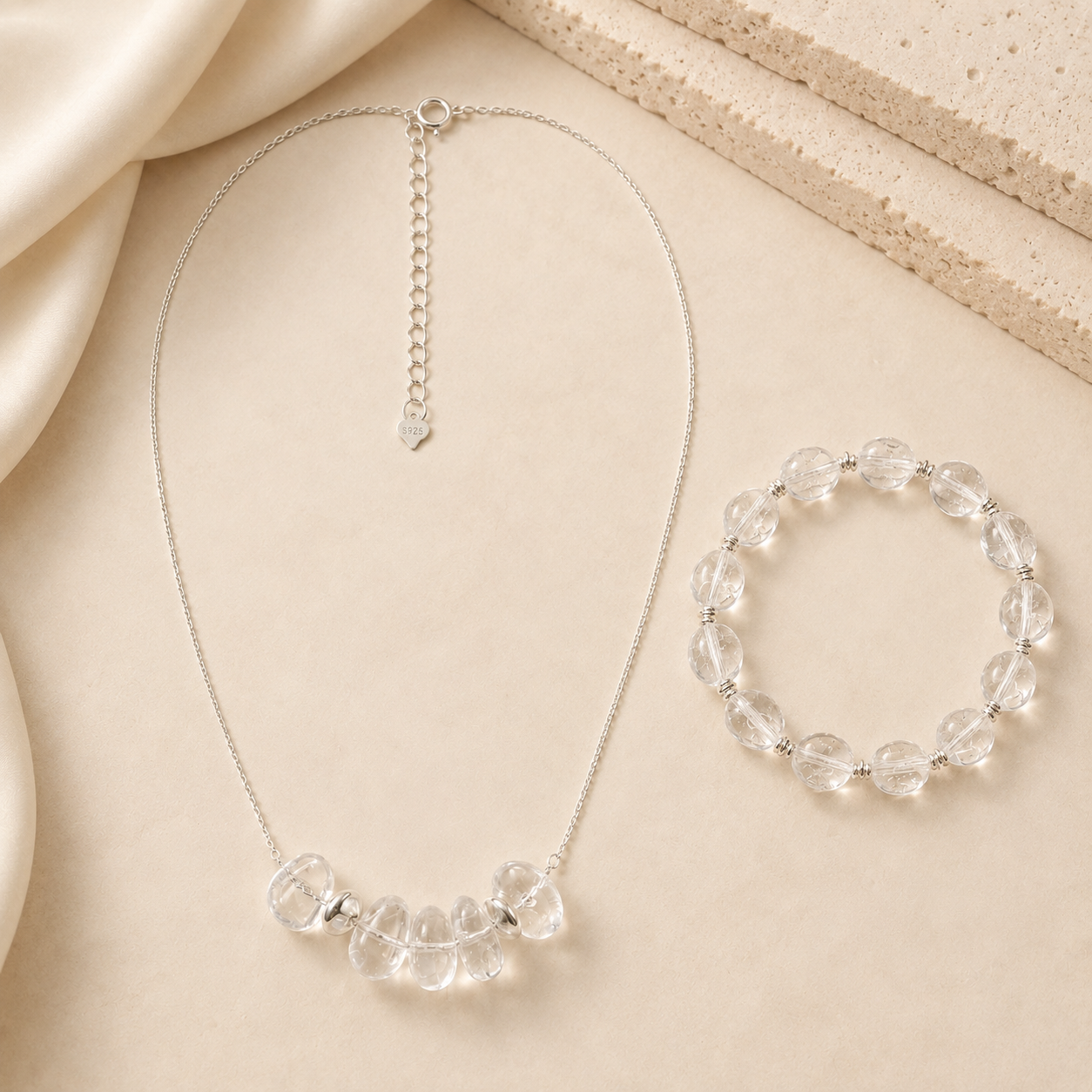 Clear quartz pendant necklace and clear quartz bracelet styled on warm ivory fabric for the LUNARAE Clarity collection.