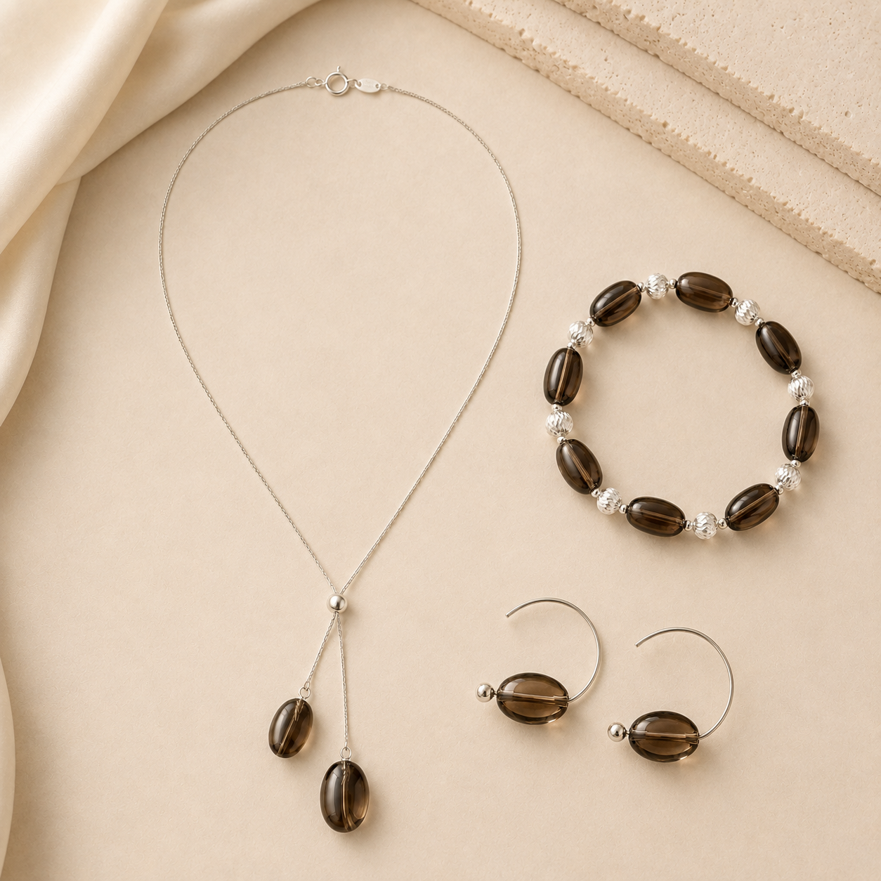 Smoky quartz necklace, bracelet, and earrings arranged on a warm neutral background for the LUNARAE Grounding collection.