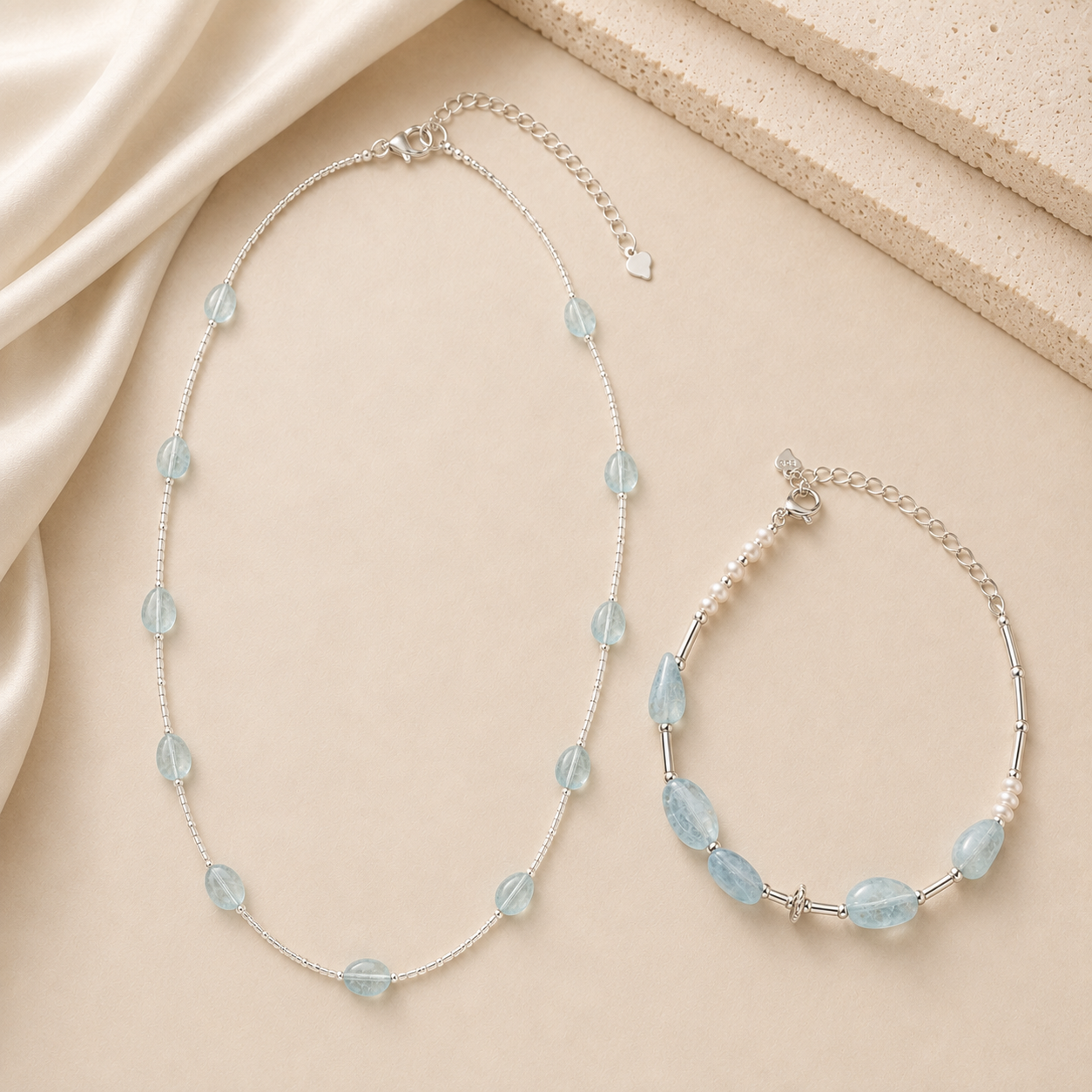 Aquamarine necklace and aquamarine pearl bracelet styled on warm ivory fabric for the LUNARAE Softness collection.