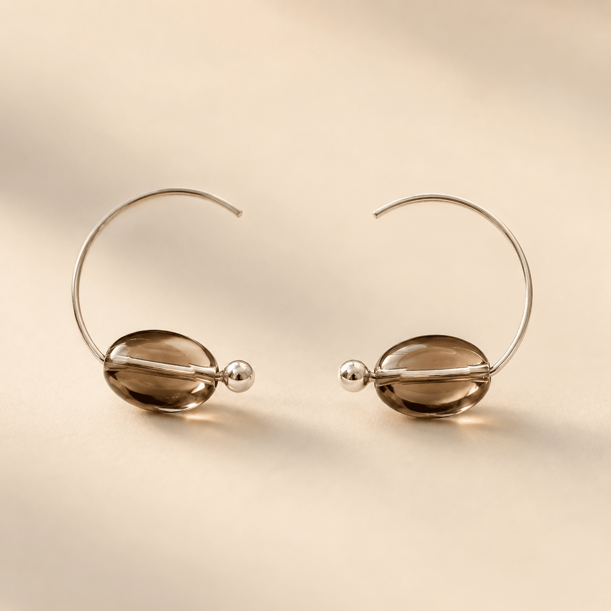 Smoky Quartz Hoop Earrings displayed as a pair on a warm ivory background with oval smoky quartz beads and polished sterling silver hoops