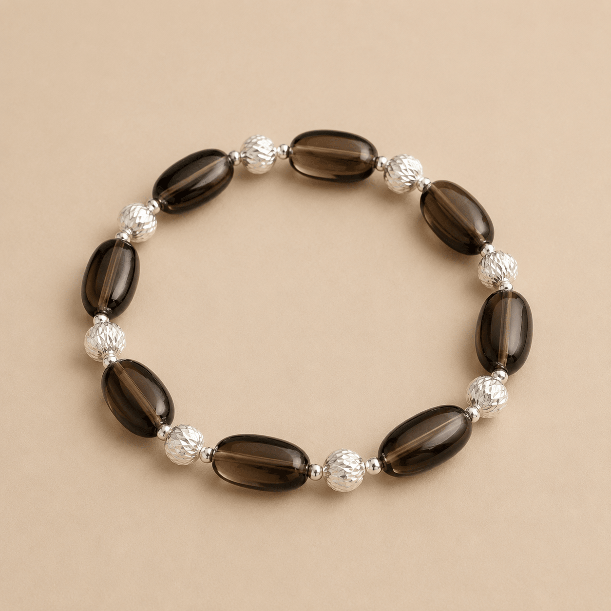 Smoky Quartz Stretch Bracelet displayed on a warm ivory background with oval smoky quartz stones, textured sterling silver beads, and small polished silver spacers