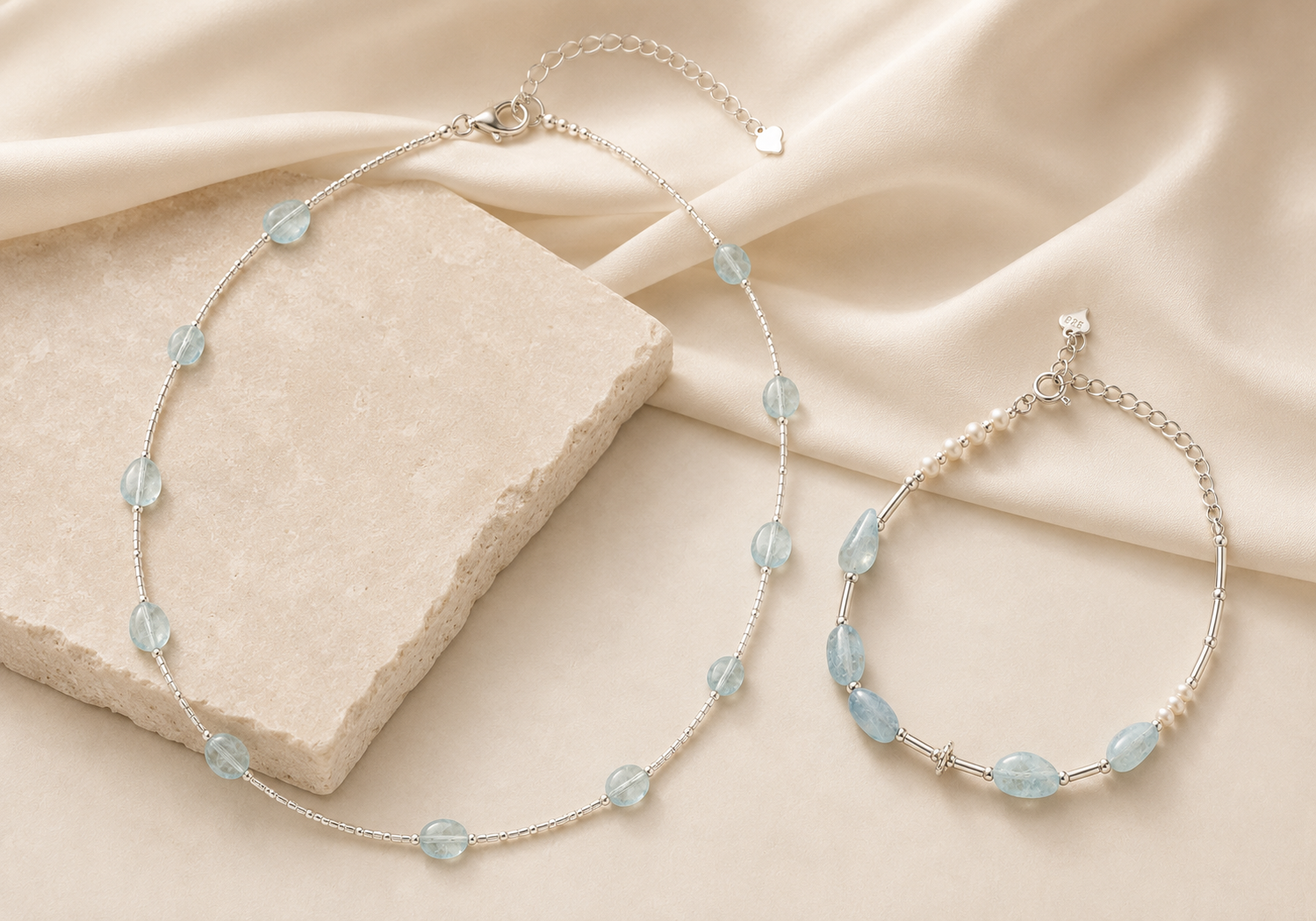 Aquamarine tube necklace and aquamarine pearl bracelet from the LUNARAE Softness Collection styled on warm ivory stone and satin.